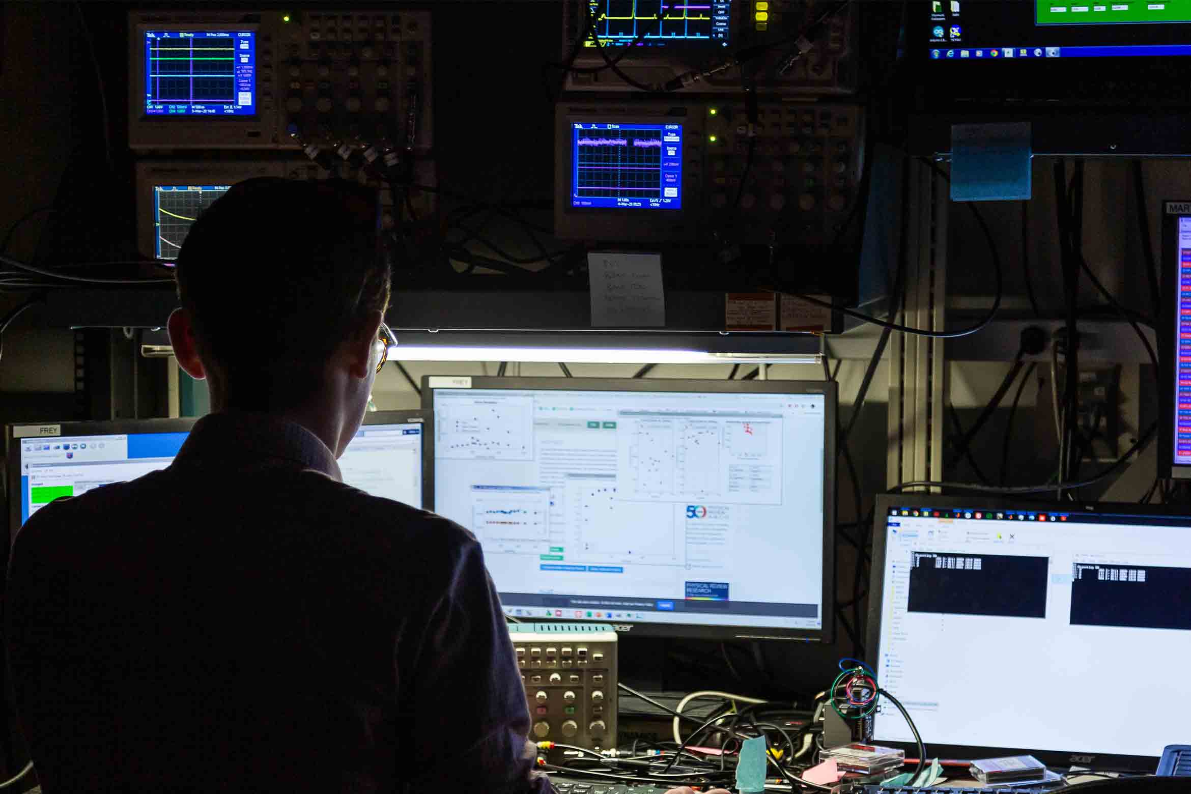 A man seated with 3 computer screens in front of him.